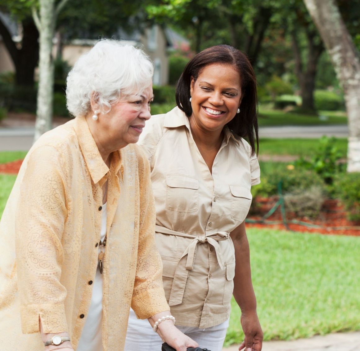 Walks & mobility support Caregiver walking arm-in-arm with a senior outdoors for a gentle neighborhood stroll.
